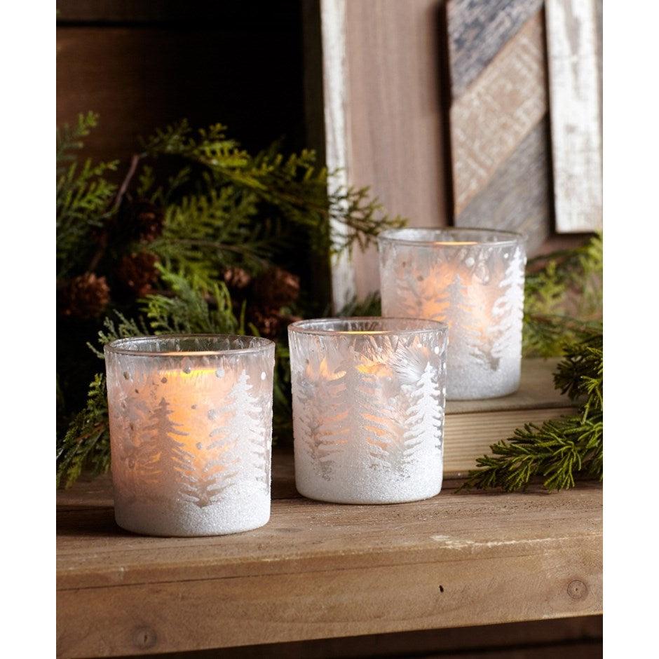 Three snowflake candle holders on a wooden table.