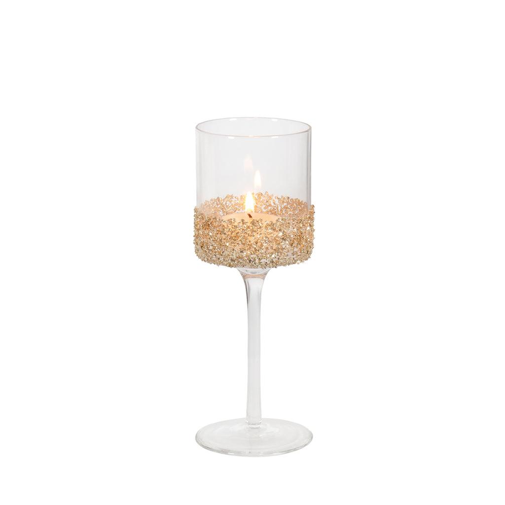 Enhance your space with the subtle elegance of our Small Clear Glass Tealight Holder. Standing gracefully on a stem, this candle holder is 7.75 inches tall and exudes a touch of sophistication. It features a delicate gold glass glitter band that adds a hint of sparkle to your décor, making it perfect for special occasions or everyday use.